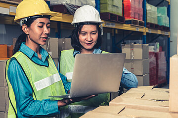 Two female warehouse workers using a laptop working at a storehouse. 